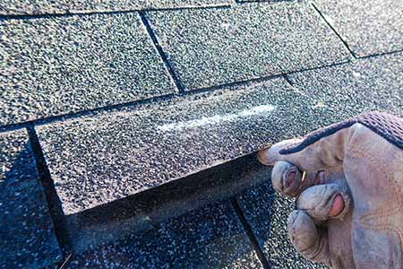 roofer inspecting hail damage shingles